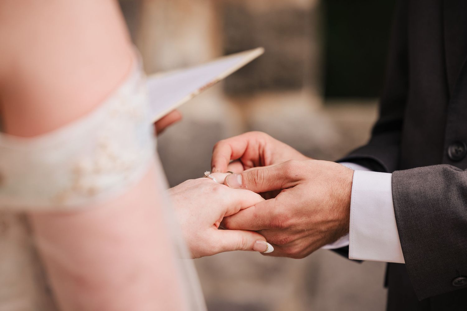 Groom placing the wedding ring on the bride's finger during the ceremony, bride holding her handwritten vows nearby.