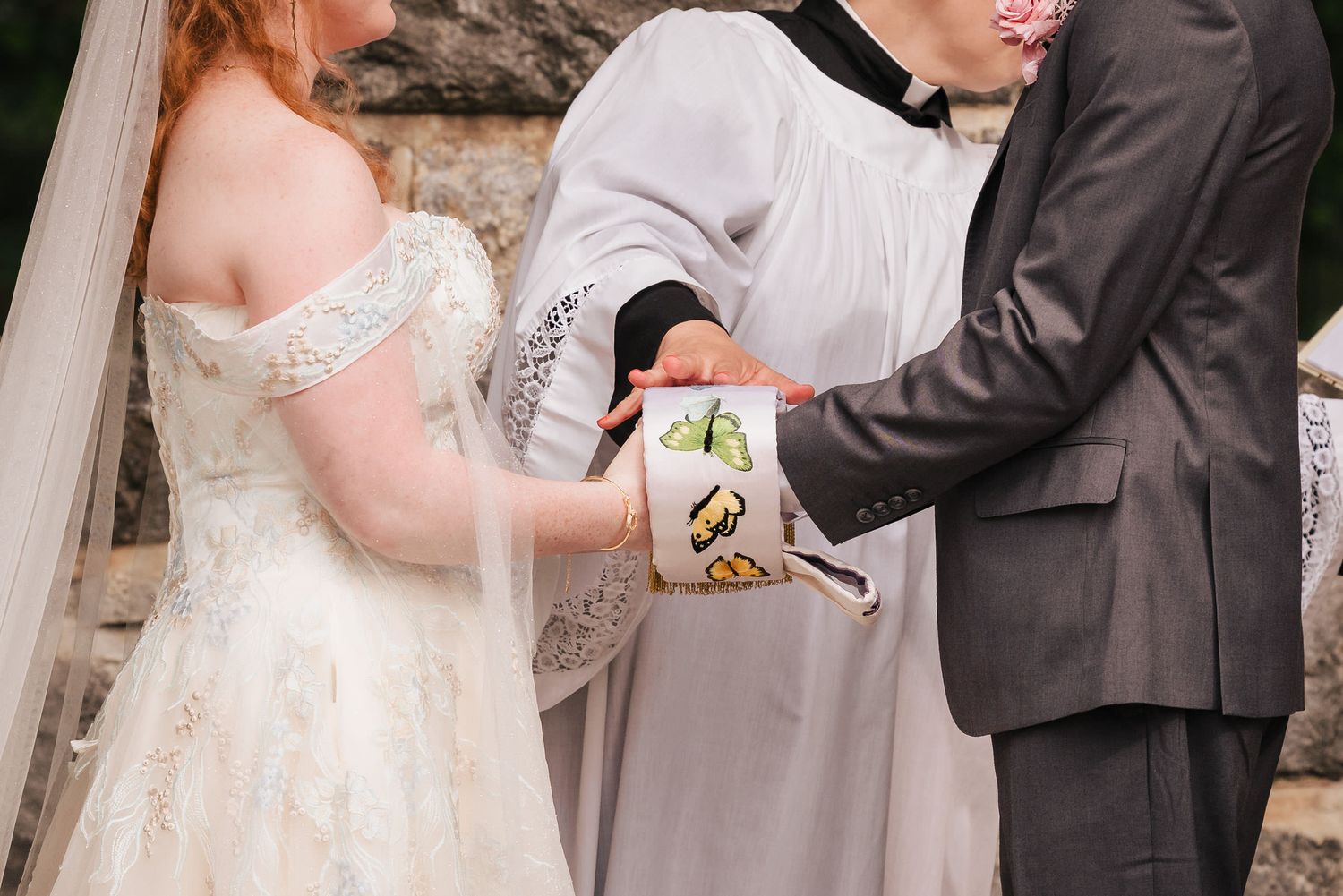 Officiant binding the couple's joined hands with a butterfly-embroidered stole during a handfasting ritual at Searles Castle in Windham, NH.