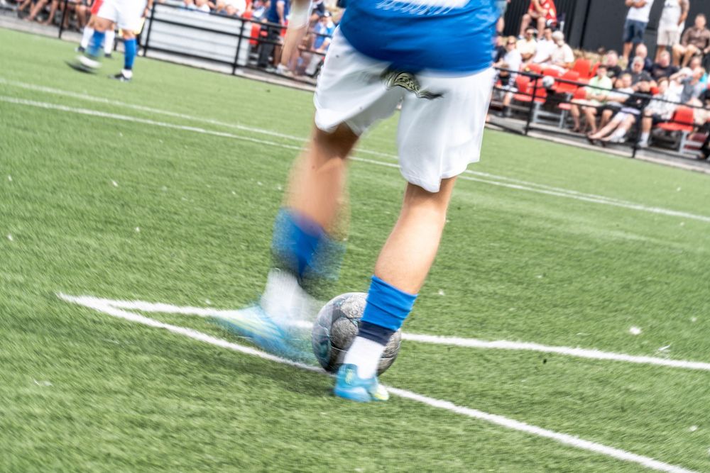 Close-up of a soccer player kicking a ball on a green turf field, wearing blue cleats and white shorts.