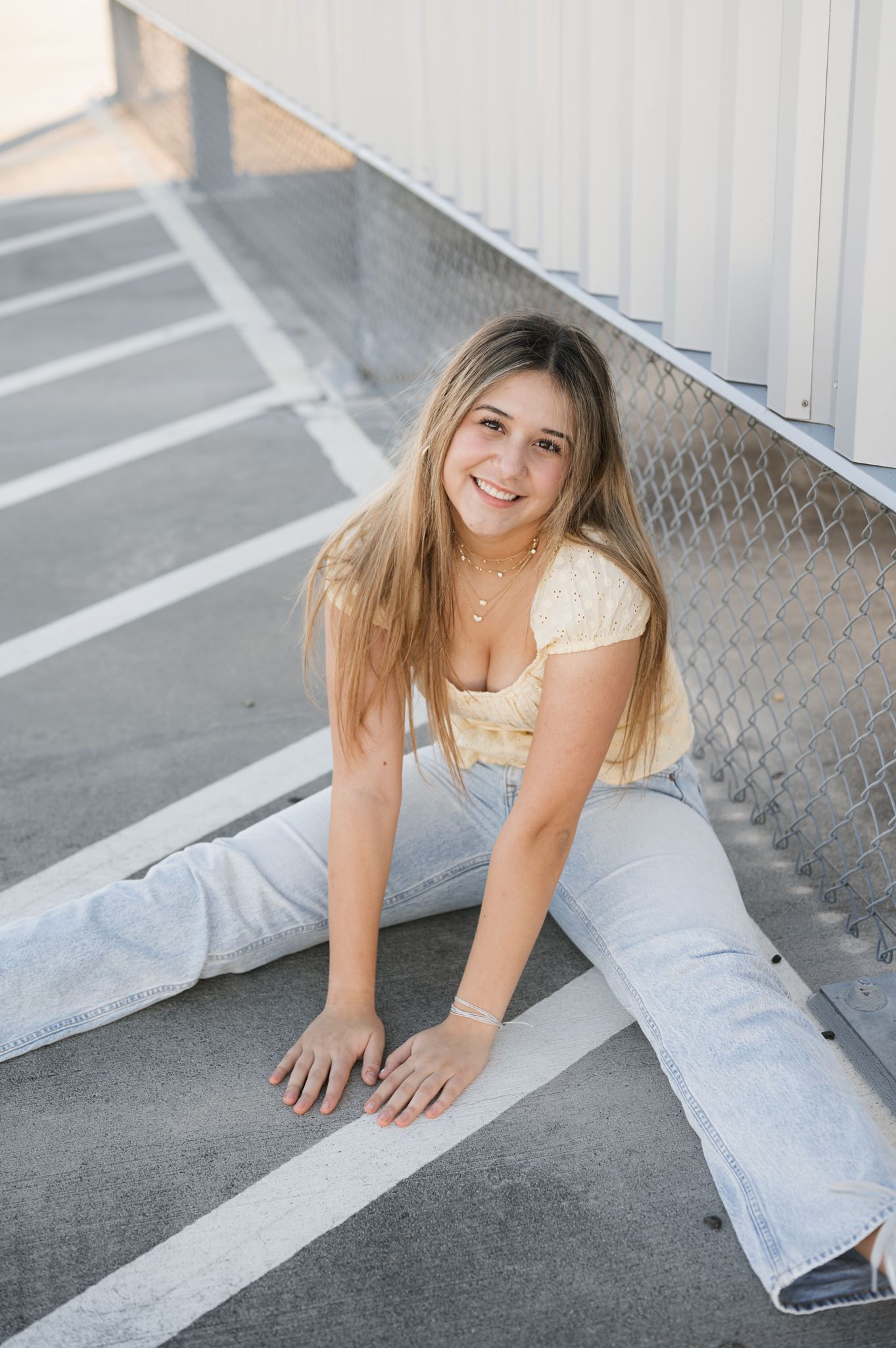 High school senior girl sitting on ground of parking garage for senior portraits