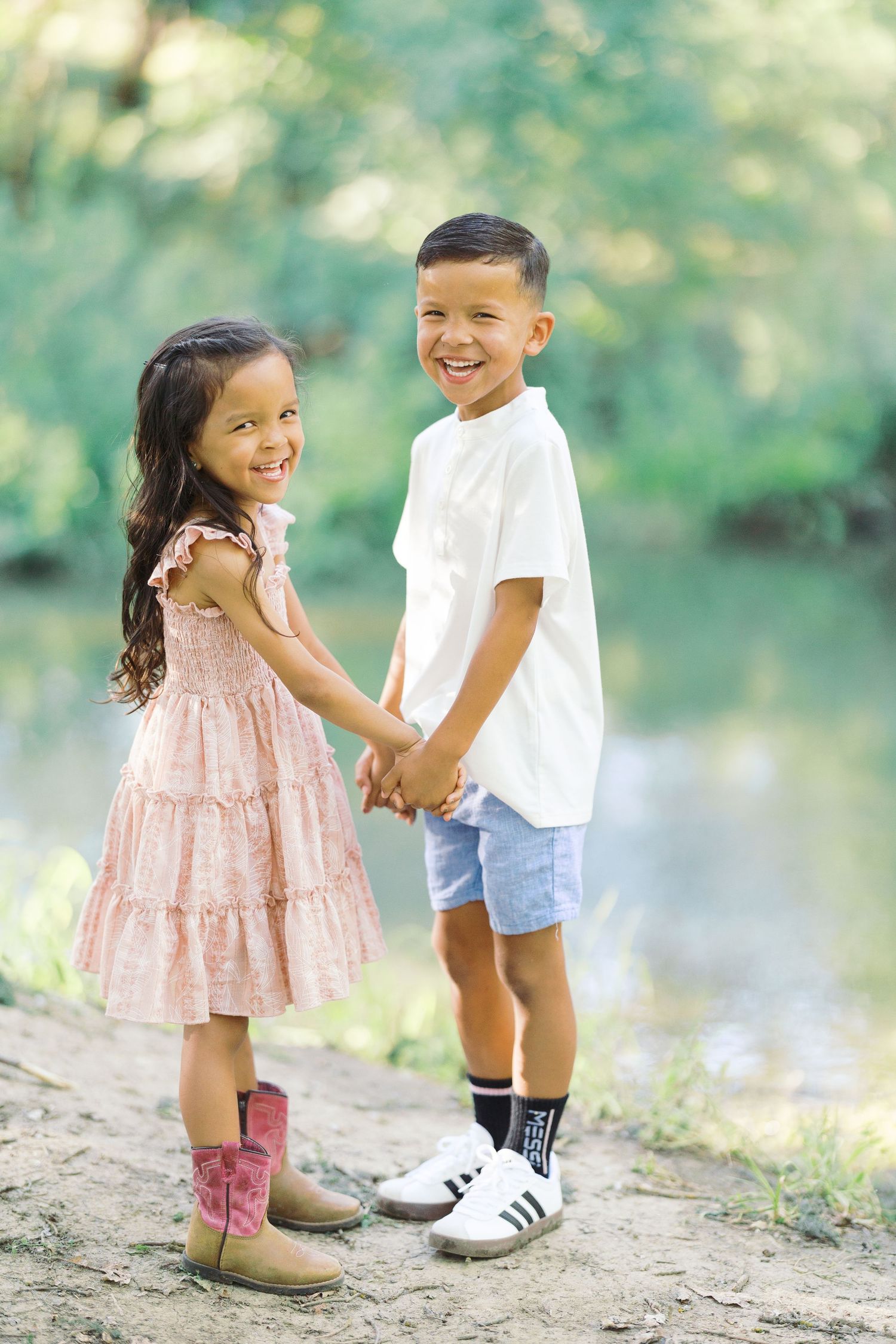 Two smiling children hold hands outdoors near a creek in Davis California during a fall mini session with Jessica Heuer Photography.