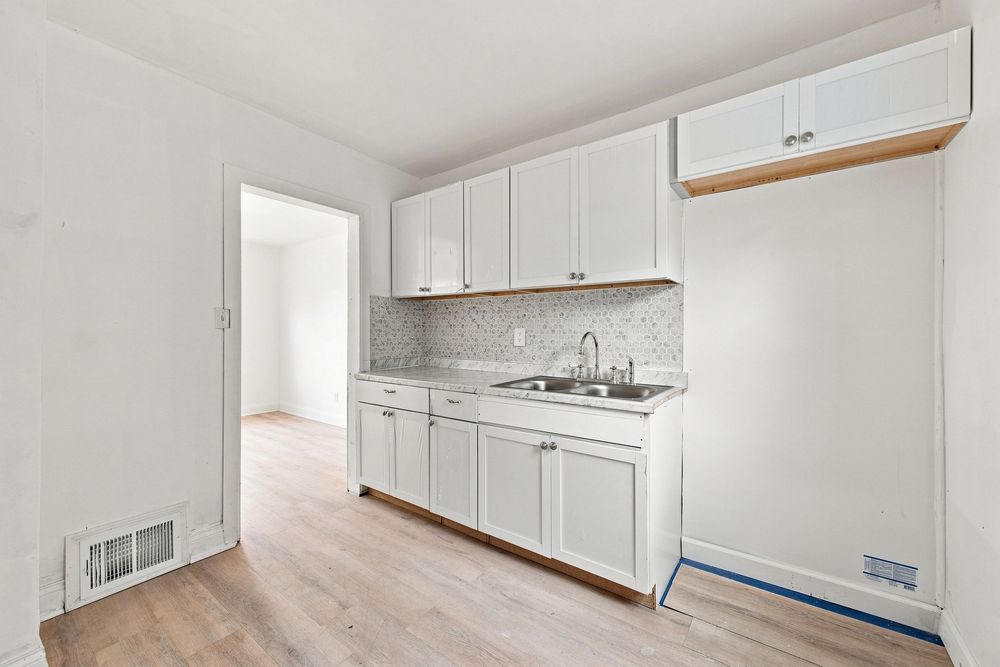 White kitchen with sink, white cabinets, mosaic tile backsplash, and light hardwood floors in a bright, clean space.