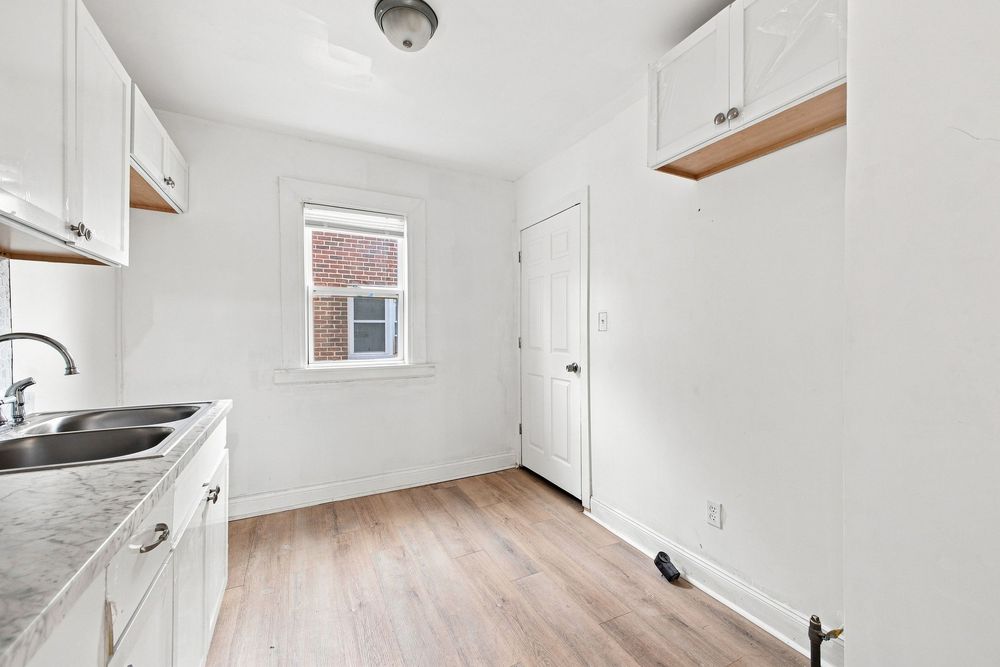Bright kitchen with white cabinets, sink, light wood floors, and a window overlooking brick building.