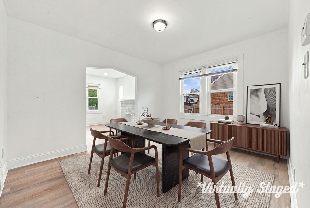 Virtually staged dining room with dark wood table, mid-century chairs, hardwood floors, and bright window overlooking neighborhood.