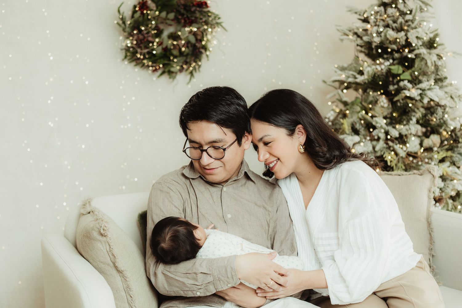 Happy couple smiling at their newborn baby during a Christmas family photo session with festive holiday decorations.