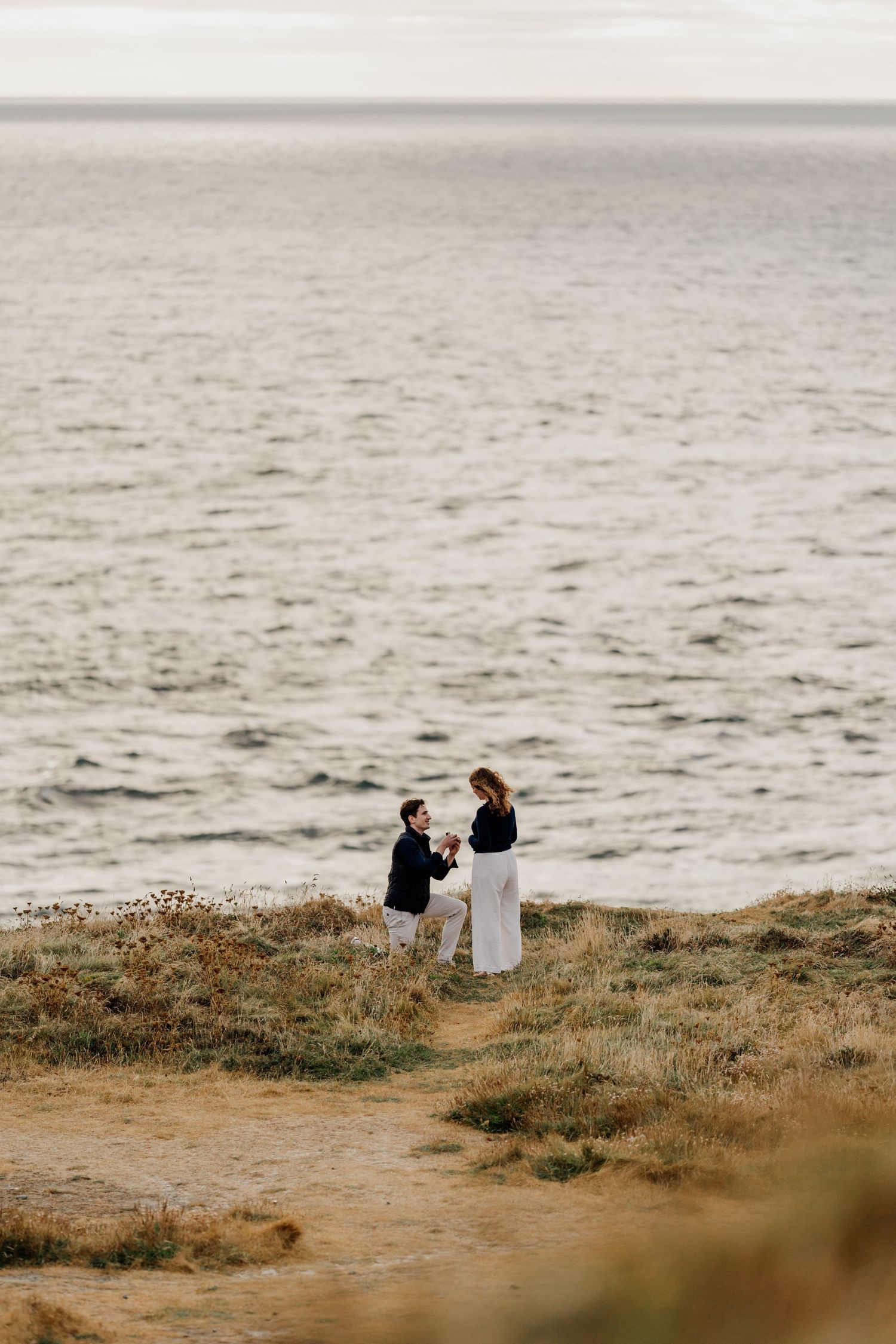 Man proposes to woman on coastal cliffside at trevose head with ocean backdrop at dusk.