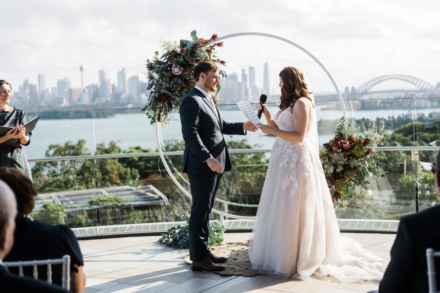 Bride and groom exchange vows at outdoor rooftop wedding ceremony with Sydney city skyline and harbour bridge backdrop.