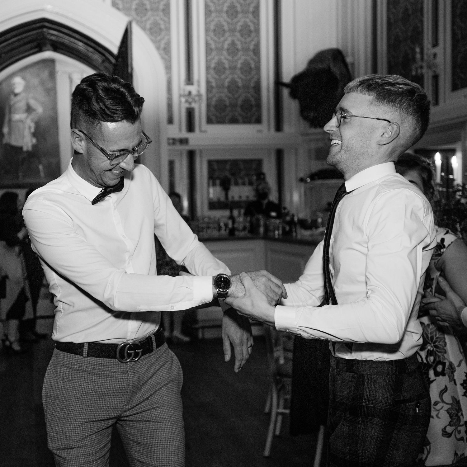 Two men in dress shirts laugh and dance together in black and white reception photo.