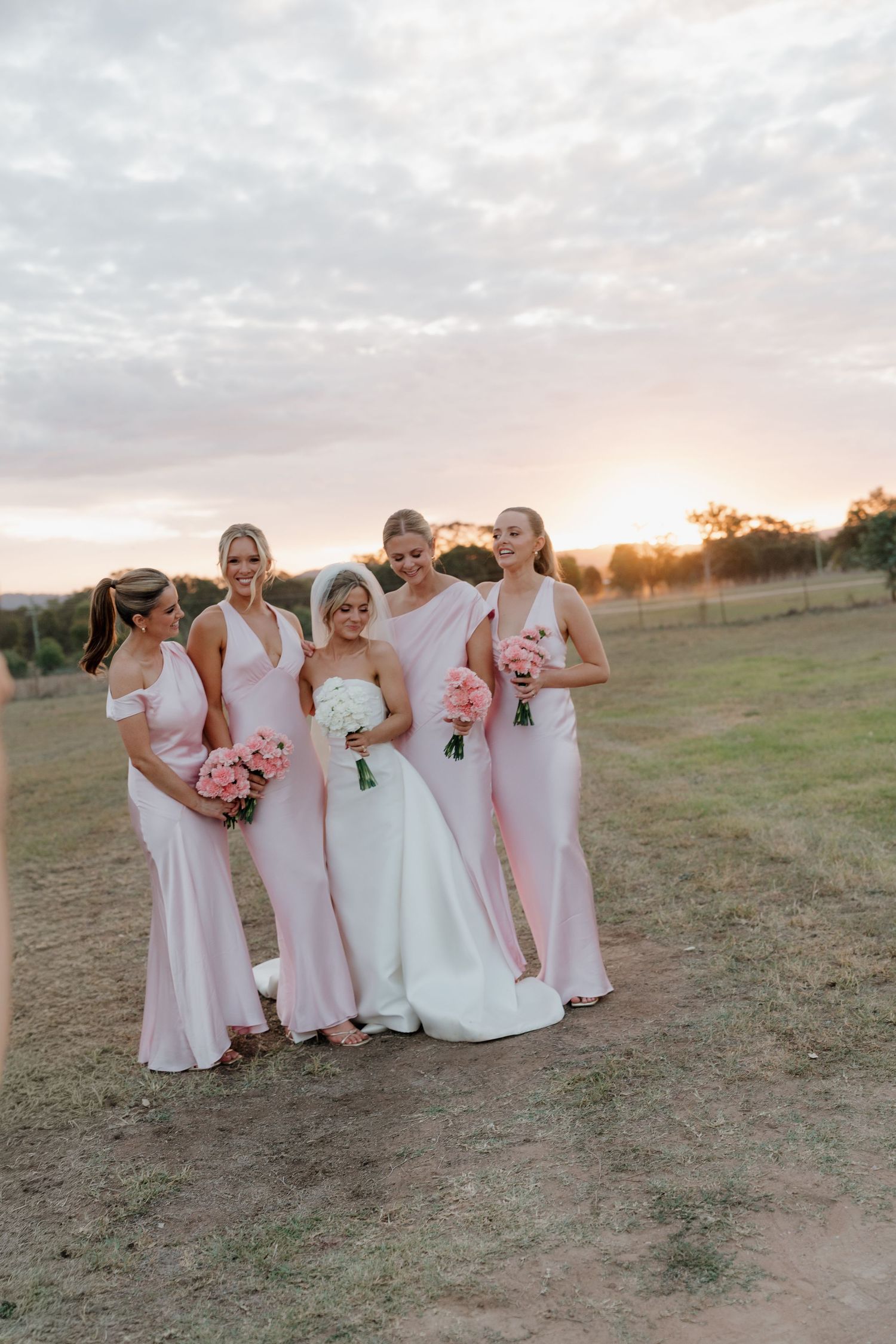 Bride in white gown with four bridesmaids in pink dresses holding bouquets at sunset.. Mudgee Wedding Photography. The Vinegrove Mudgee