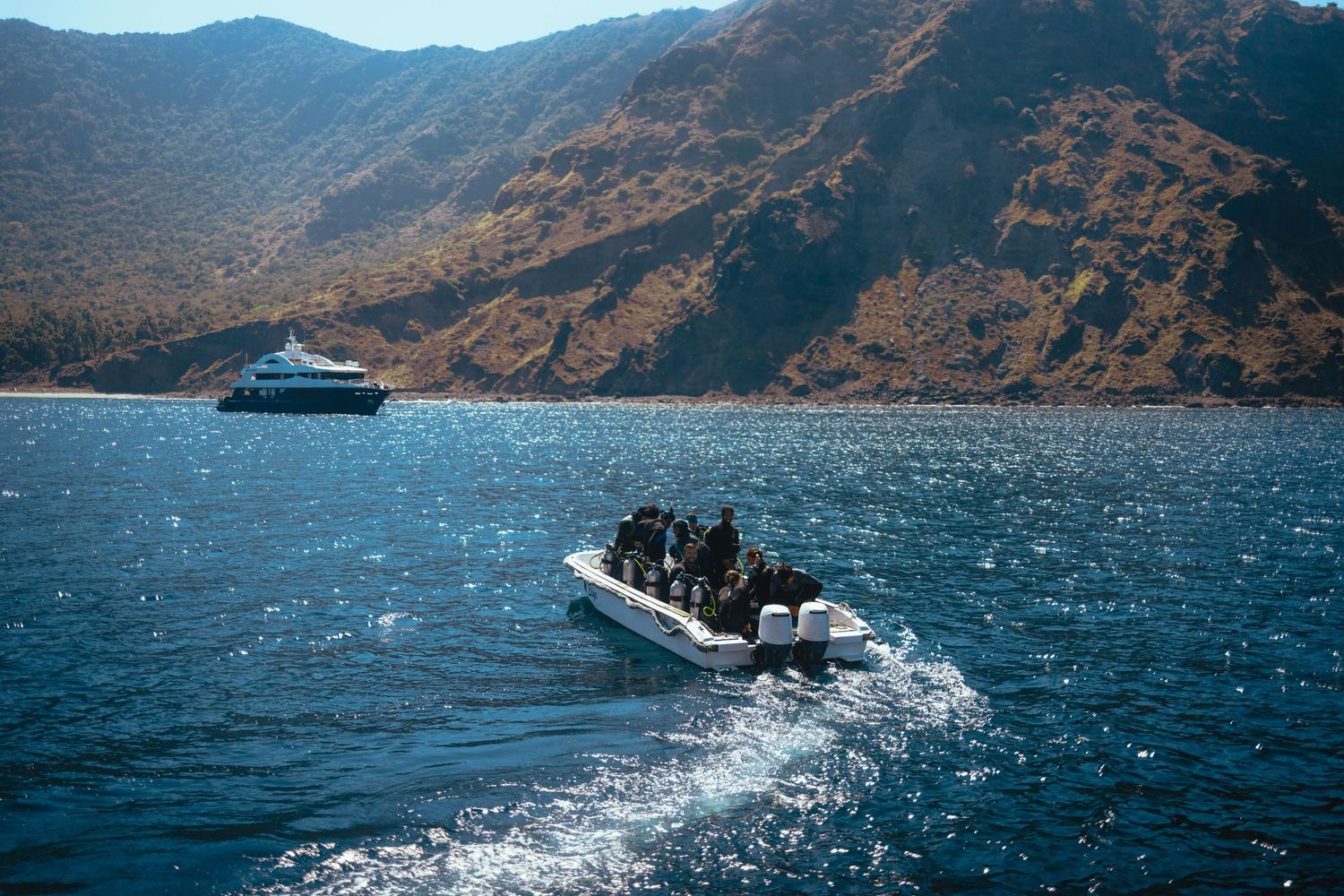 Scuba divers prepare for a night dive on a boat under a dramatic dark sky with glowing equipment lights.
