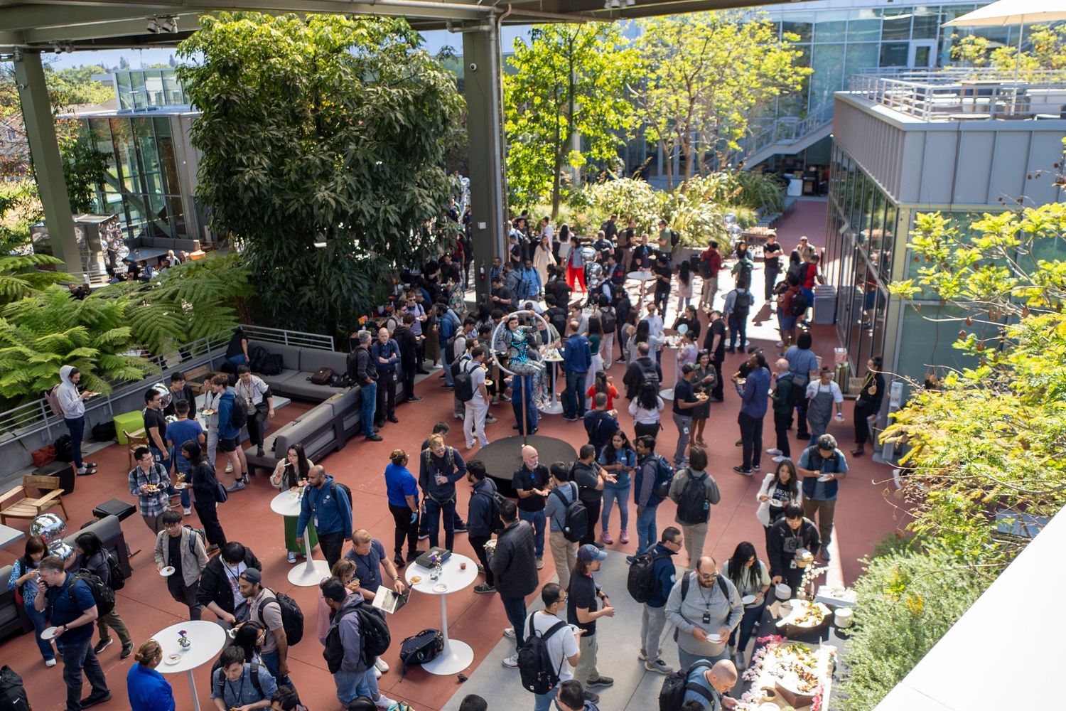 Aerial view of a large outdoor corporate networking event with crowds of professionals gathered on a modern campus plaza.