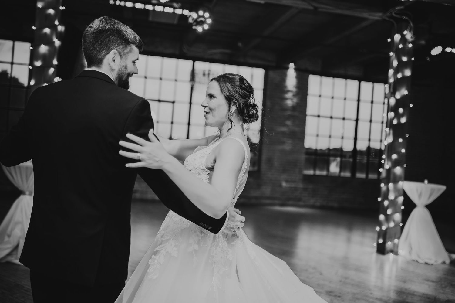 Black and white photo of bride and groom sharing their first dance at elegant wedding reception with fairy lights.