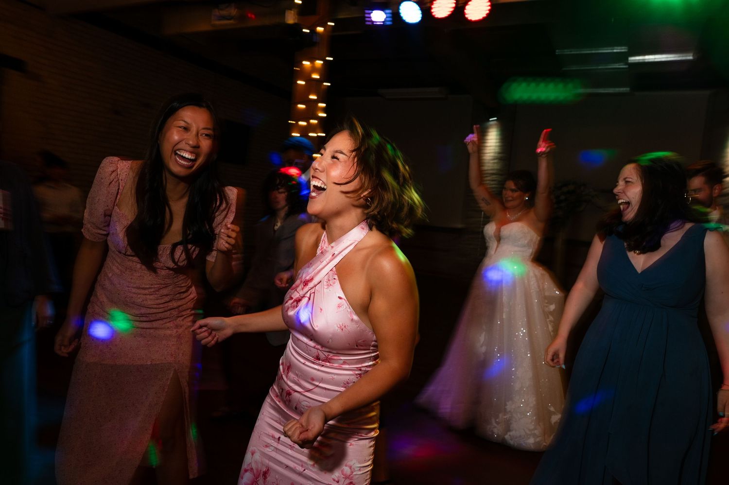 Guests dancing joyfully at wedding reception under colorful disco lights in evening celebration.