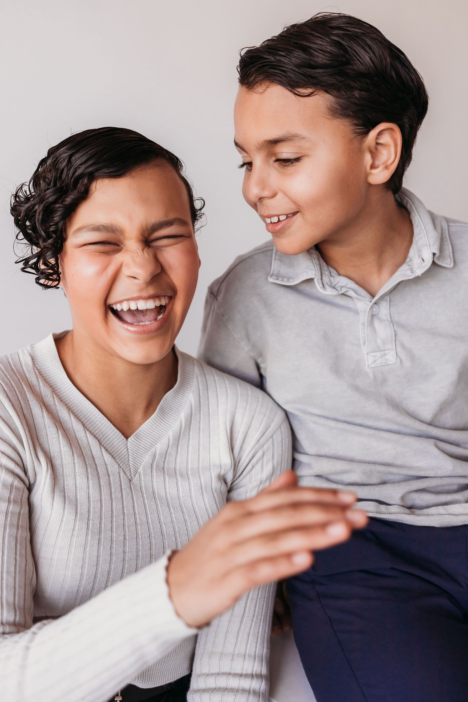 A woman and boy laughing together, sharing a joyful moment in matching gray tops against a light background.