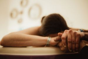 Person resting head on table during a relaxing massage therapy session, holding hands with a caring touch.