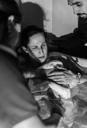 Black and white photo of a mother holding her newborn baby during a water birth, supported by medical staff.