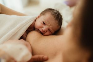 Newborn baby resting on mother's chest during skin-to-skin contact after birth, wrapped in white towel.