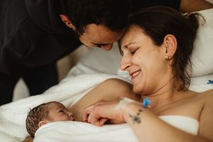 New parents share a tender moment with their newborn baby in a hospital bed after birth.