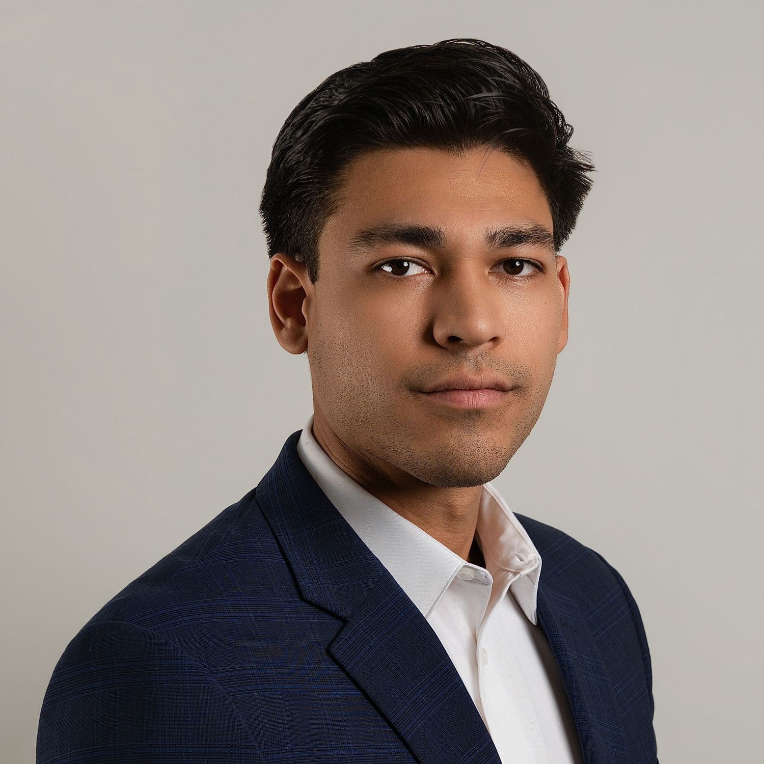 Professional headshot of a young man in a navy blazer and white shirt against a neutral gray background.