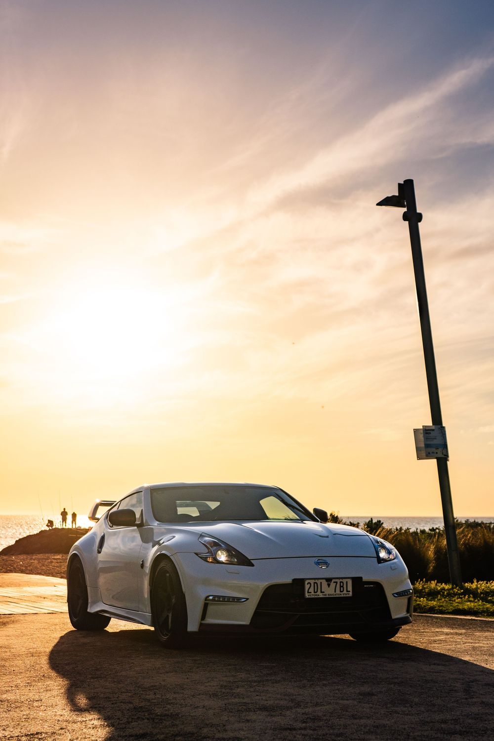 White Nissan 370Z Nismo parked at coastal lookout during vibrant golden hour sunset.