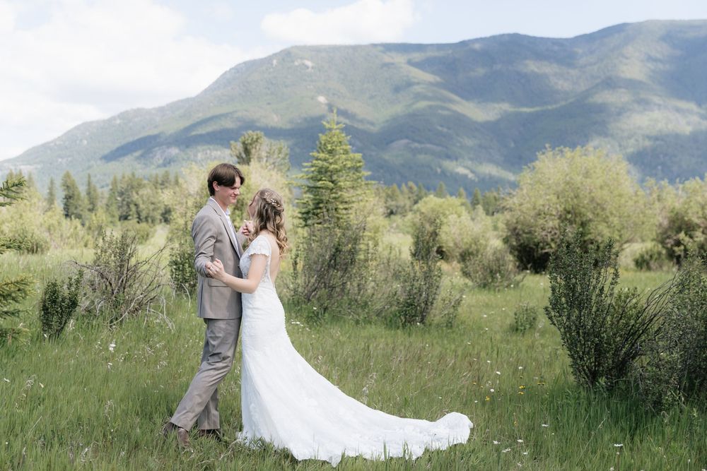 Bride and groom embrace in a lush green meadow with stunning mountain backdrop on their wedding day.