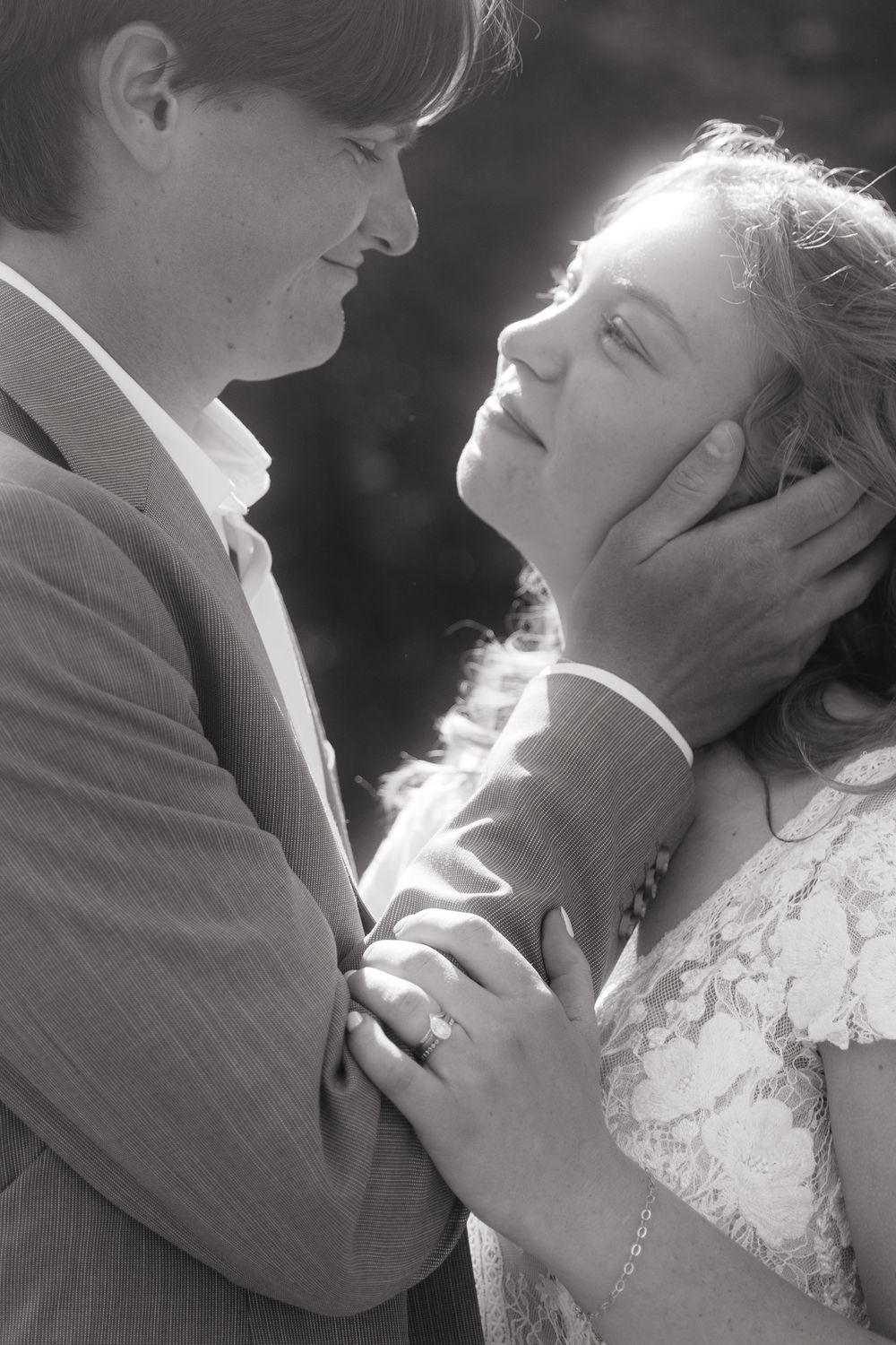 Black and white photo of a romantic couple gazing at each other, man tenderly holding woman's face outdoors.