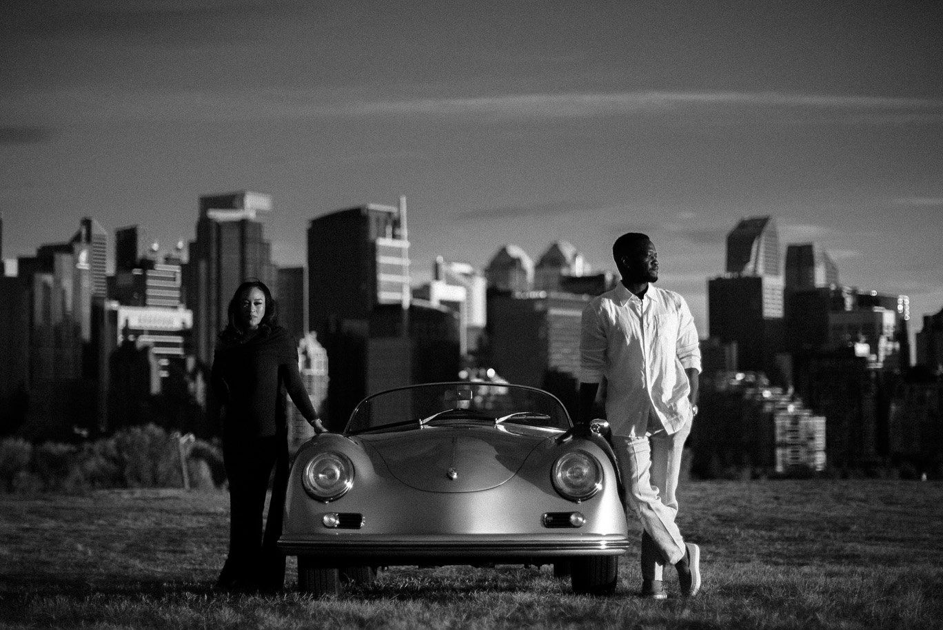 Black and white engagement photo with a classic car and the city skyline