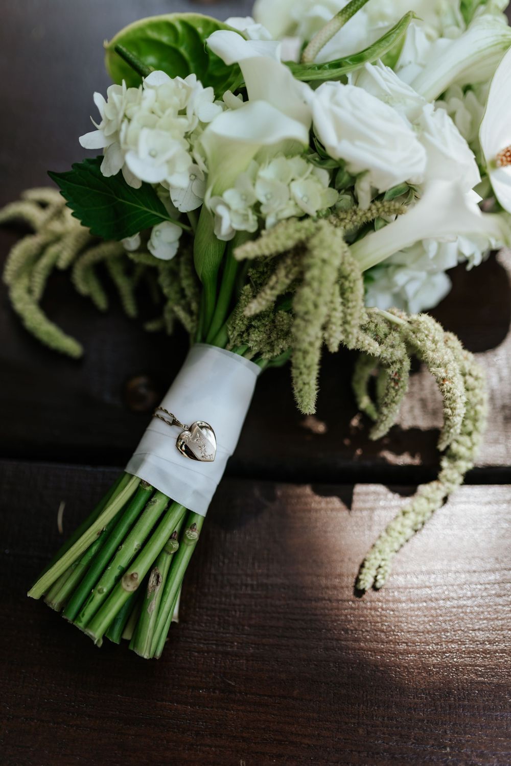 White rose and calla lily wedding bouquet with green amaranthus, wrapped in white ribbon with a heart locket charm.