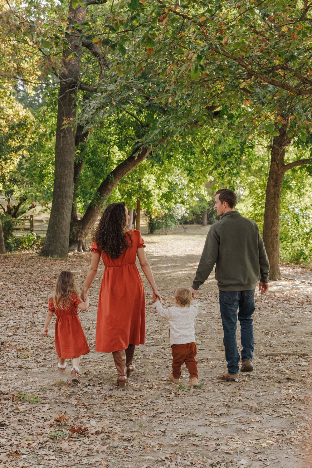 Family walking together on tree-lined path during autumn with fallen leaves.