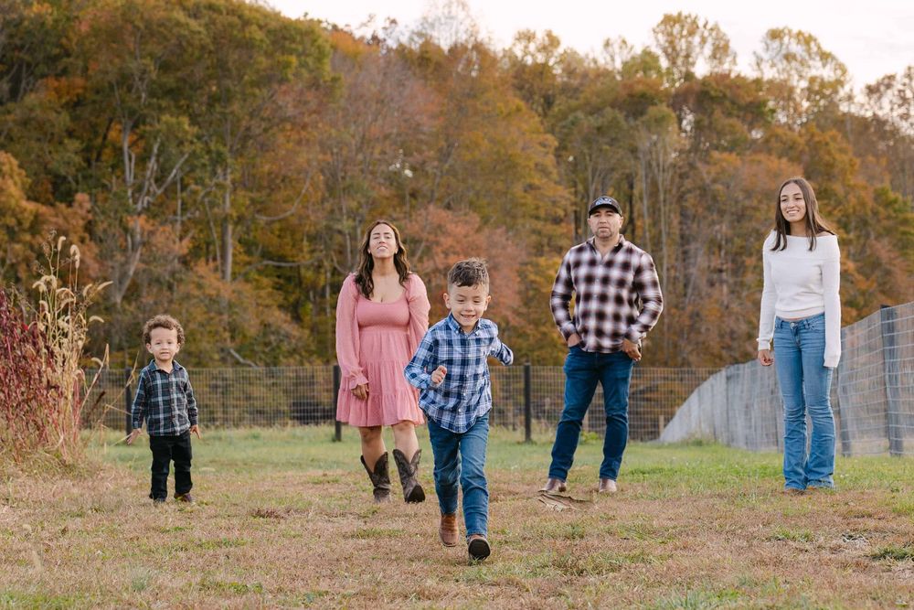 A family walking through a scenic autumn field with golden trees in the background.