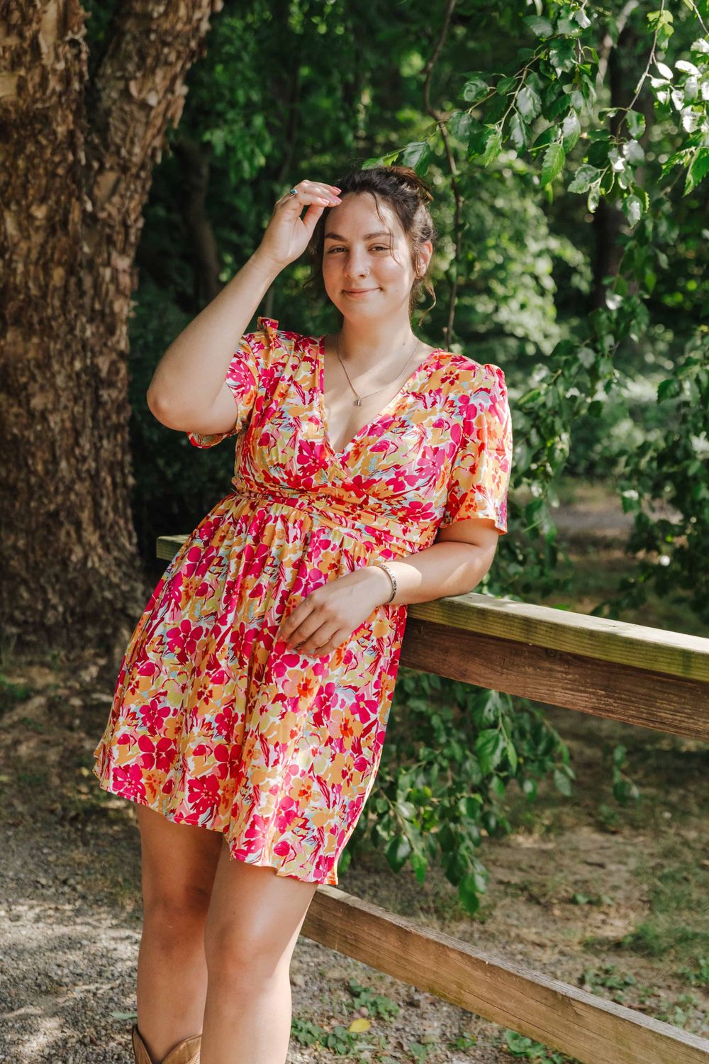 A bright floral summer dress with pink and red blooms brings cheerful color to a tranquil garden setting.