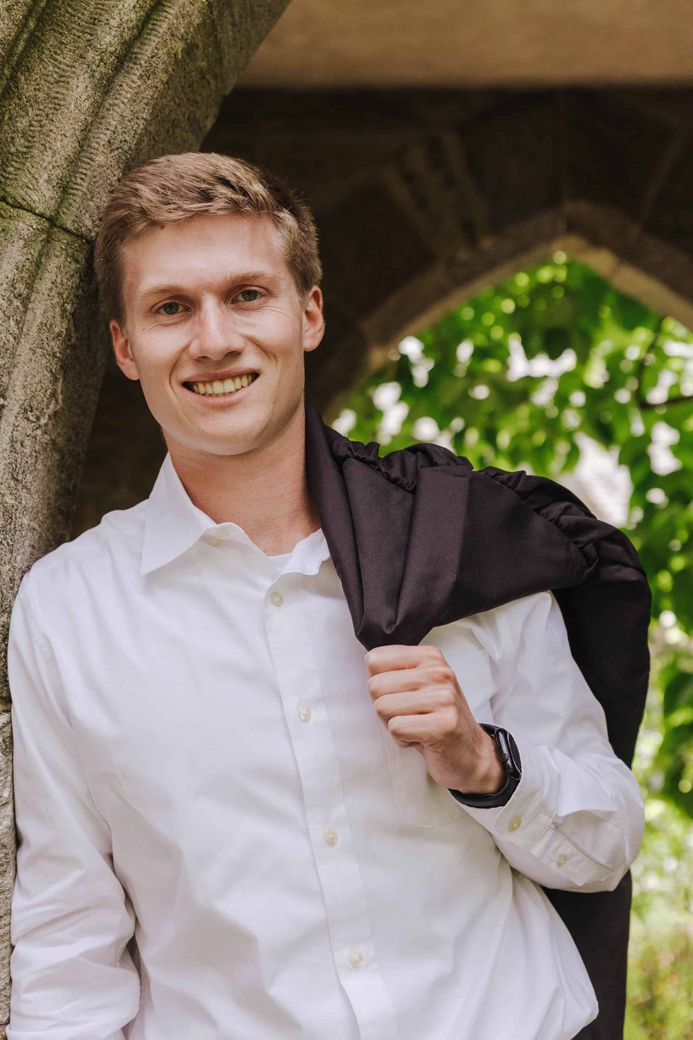 An outdoor portrait photos showing someone in a white dress shirt and black jacket against a natural background.