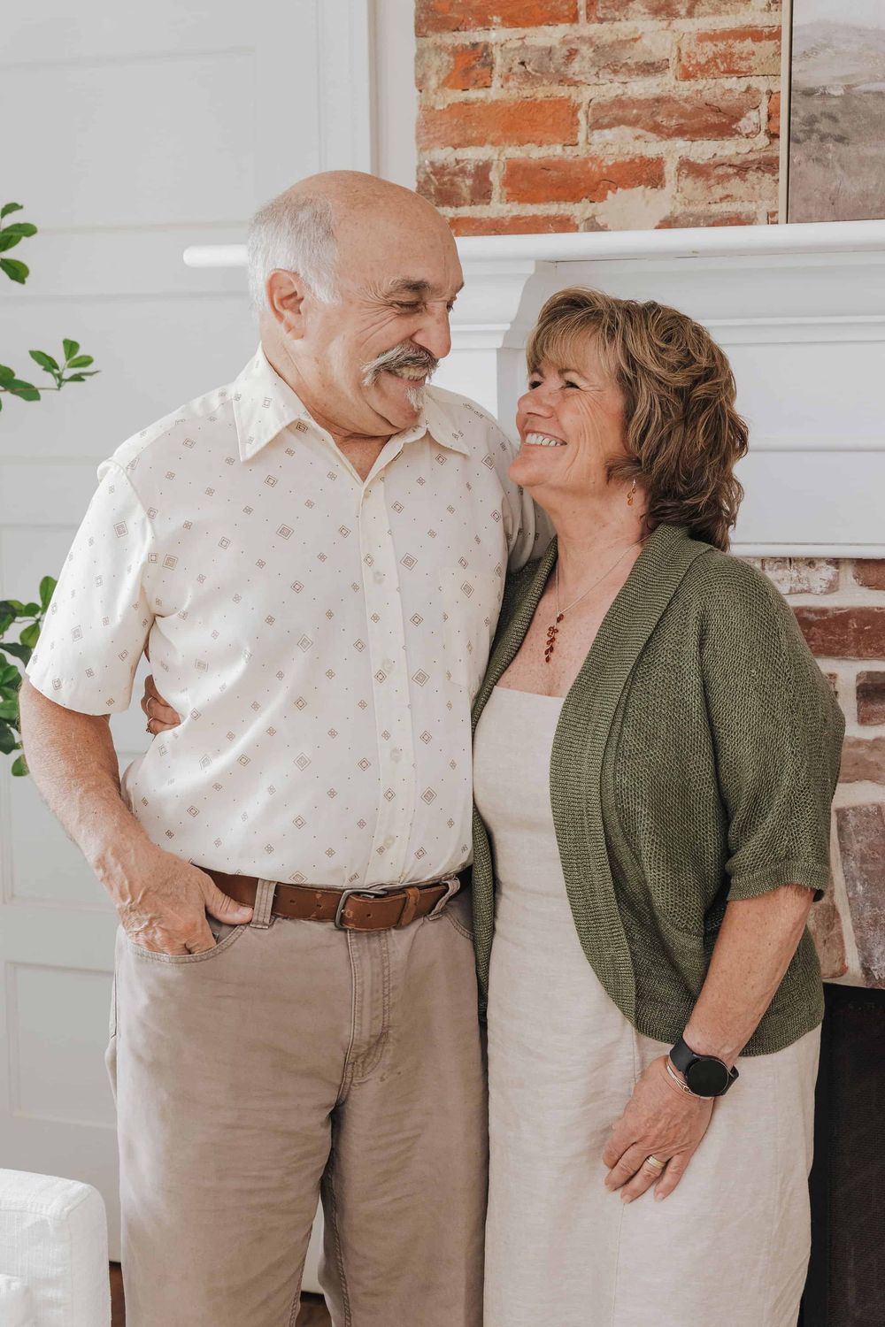 A senior couple shares an intimate moment together against a rustic brick wall backdrop.
