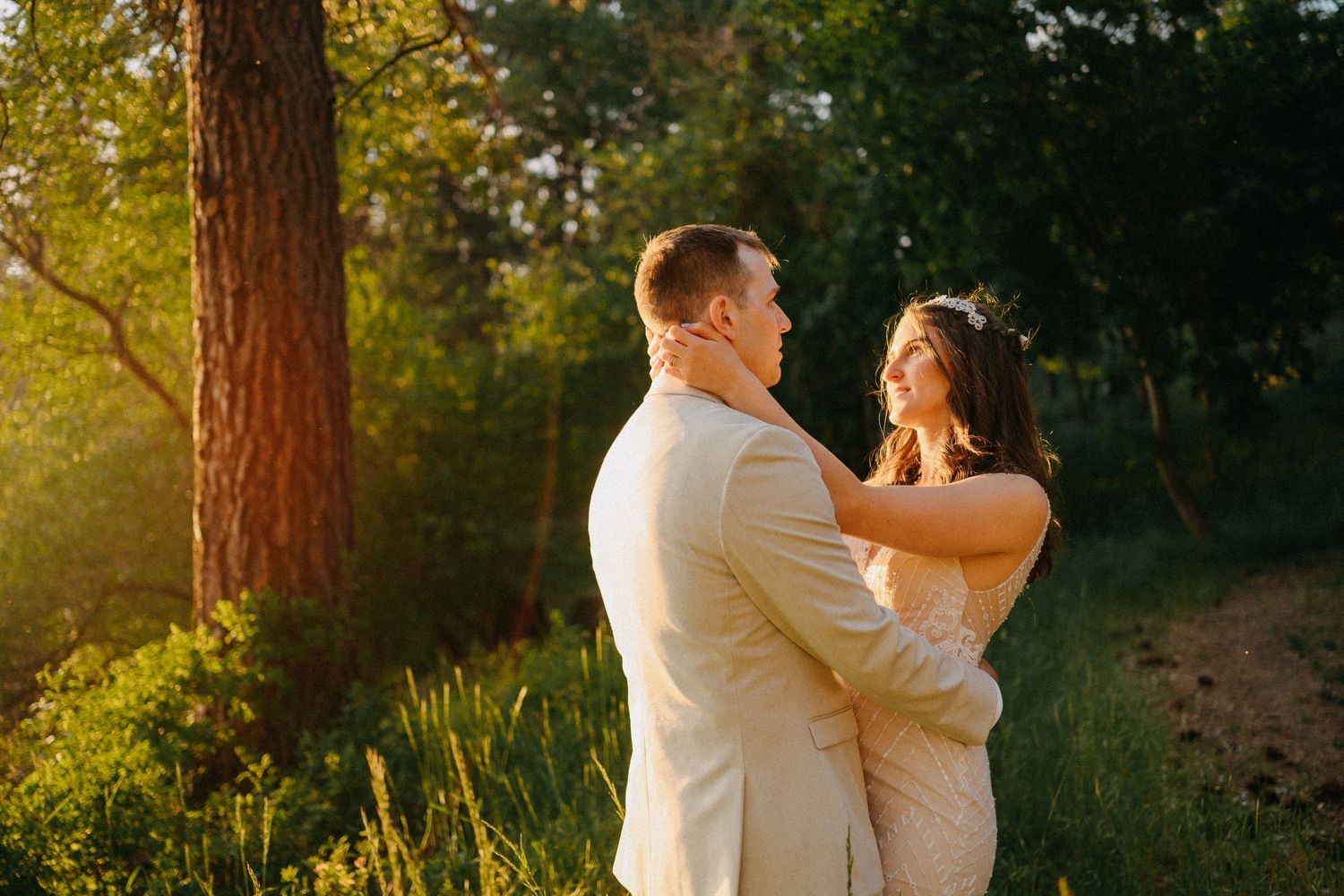 A couple shares a romantic embrace during golden hour in a sun-dappled forest setting.