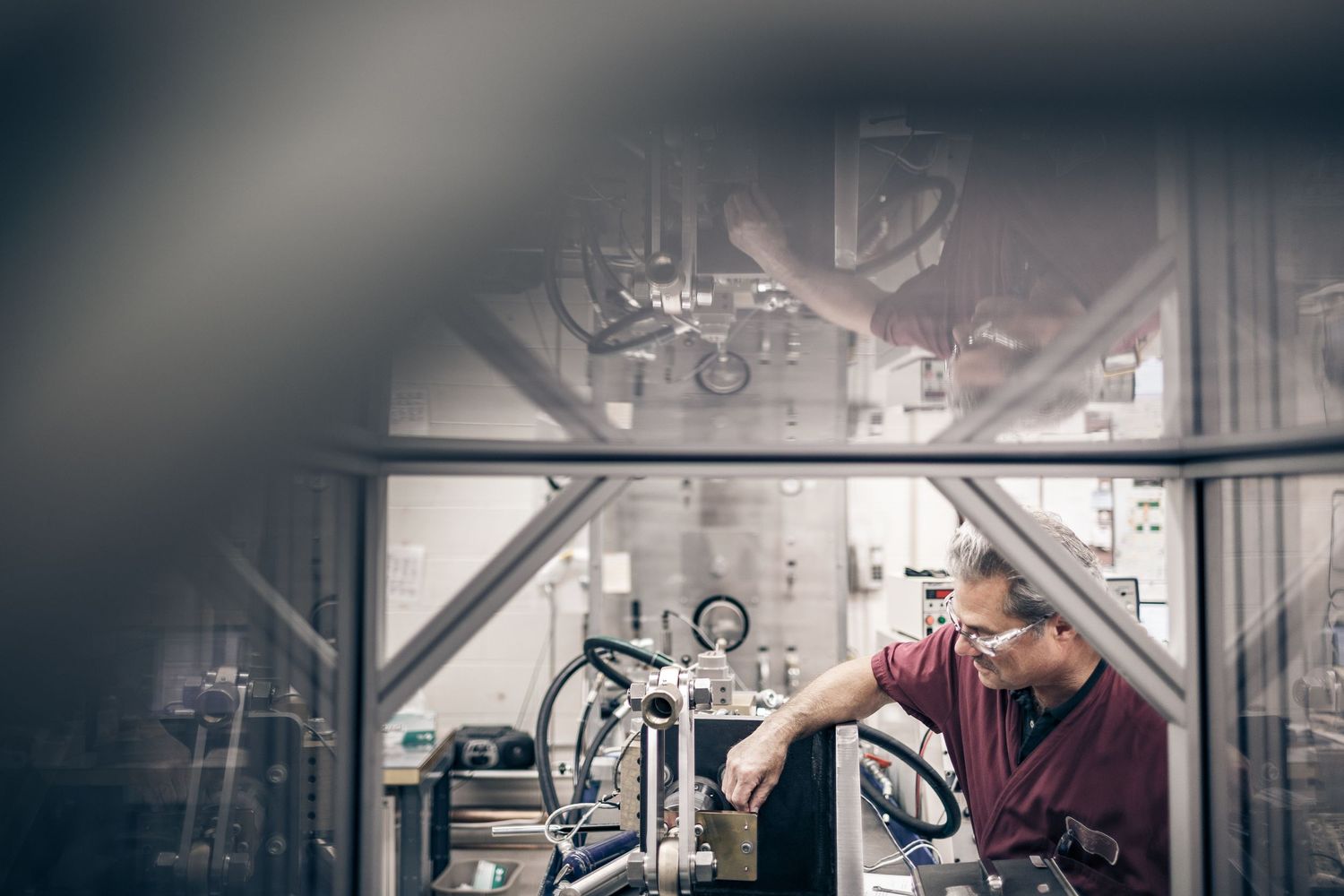 A technician in a red shirt inspects industrial brewing equipment inside a modern facility.