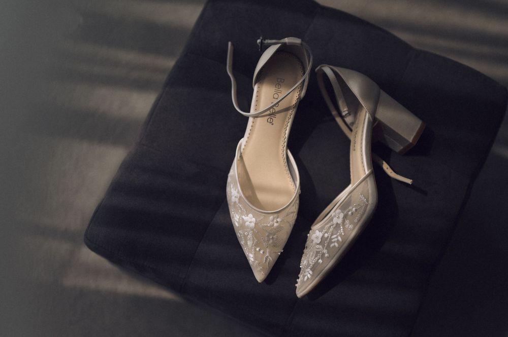 Elegant silver embroidered block heel pumps with ankle strap displayed on a dark surface.