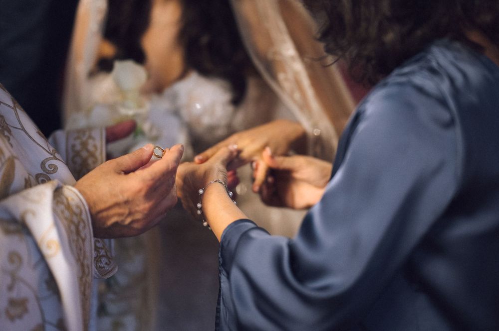 Priest placing a wedding ring on bride's finger during a traditional religious marriage ceremony.
