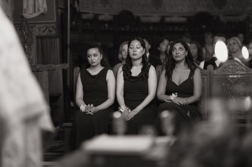 Three women in black attire stand solemnly in a church pew during a funeral service.