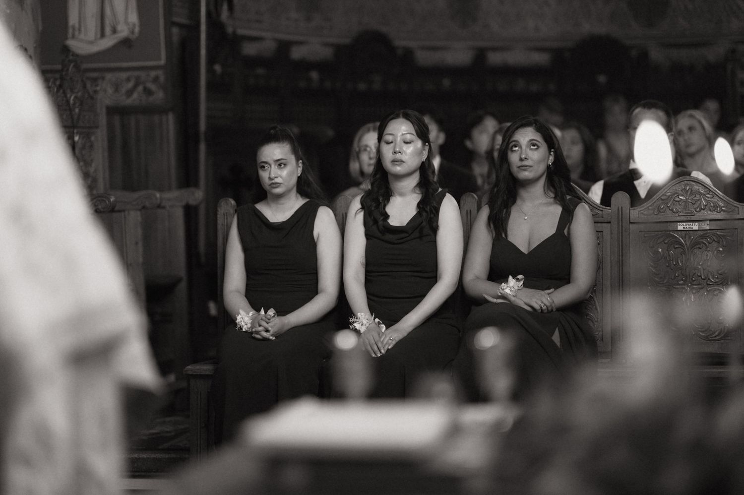 Three women in black attire stand solemnly in a church pew during a funeral service.