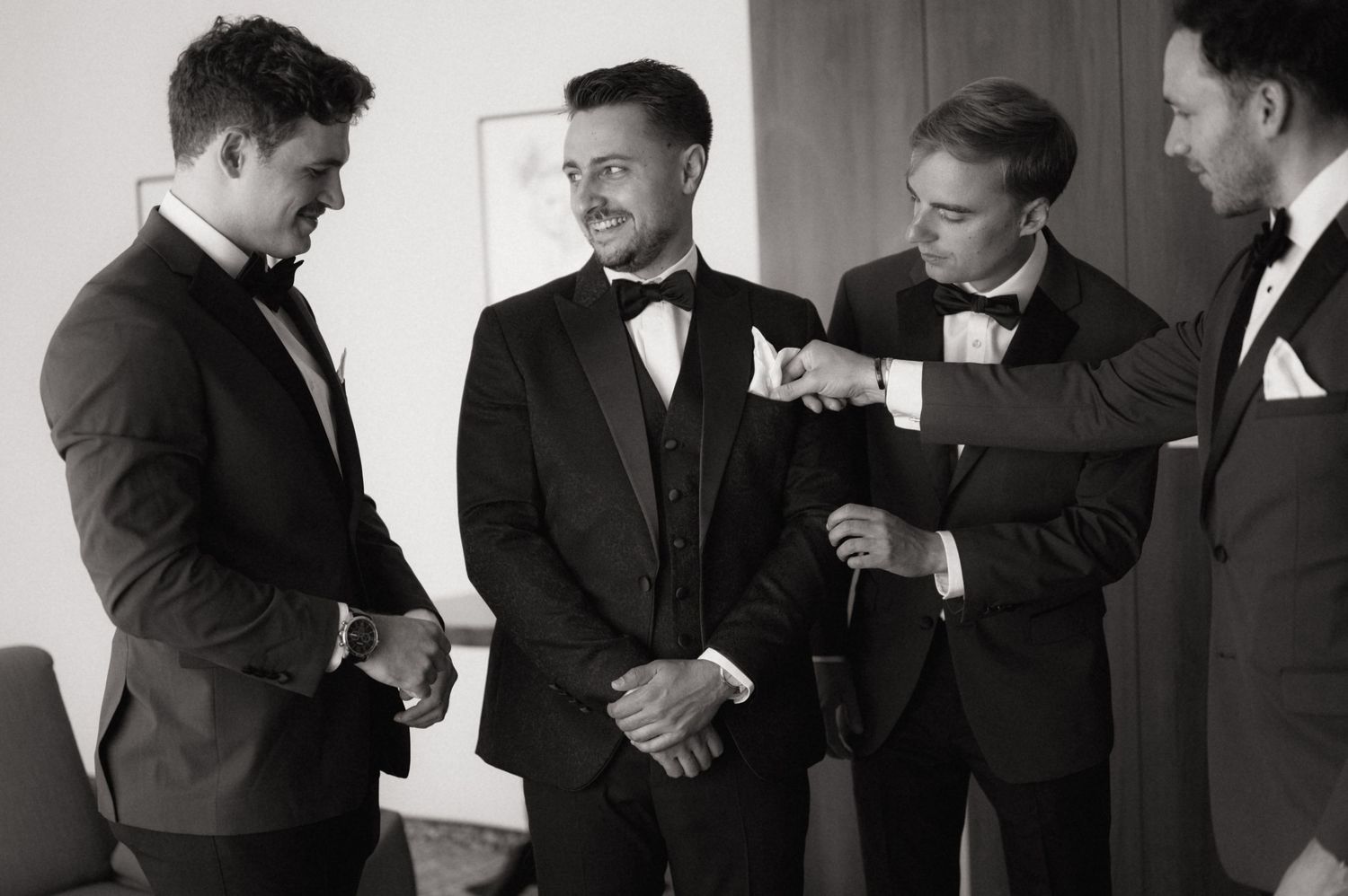 Four groomsmen in black tuxedos sharing a moment while getting ready for a wedding ceremony.