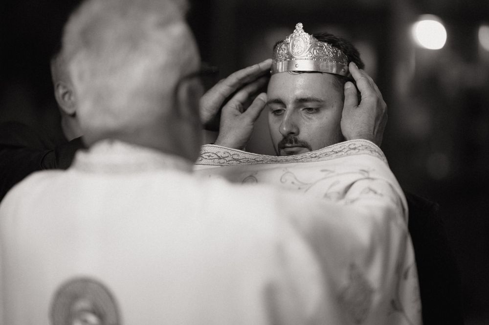 Priest placing a crown on a groom during an Orthodox Christian wedding ceremony in black and white.