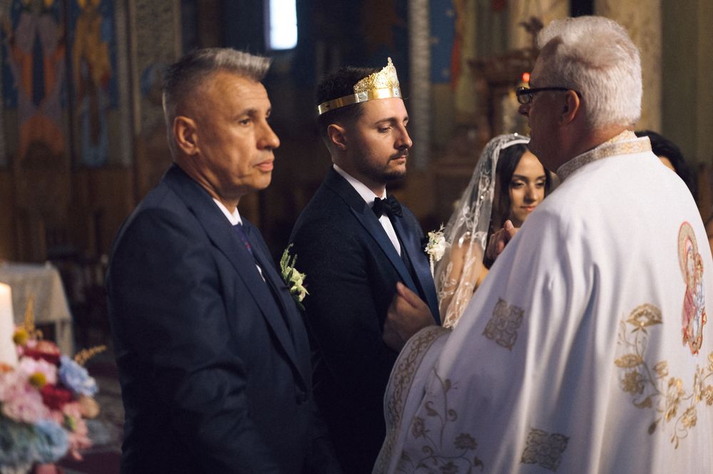 Groom with best man and bride receiving blessings from a priest during an Orthodox church wedding.