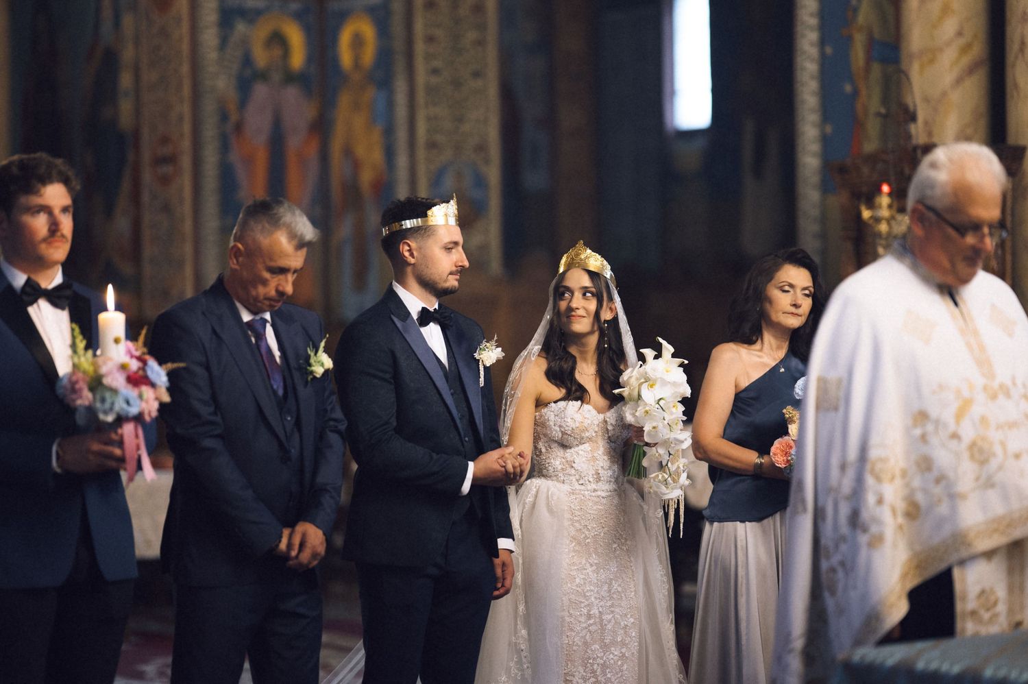 Bride and groom stand at church altar during Orthodox wedding ceremony with guests holding candles.