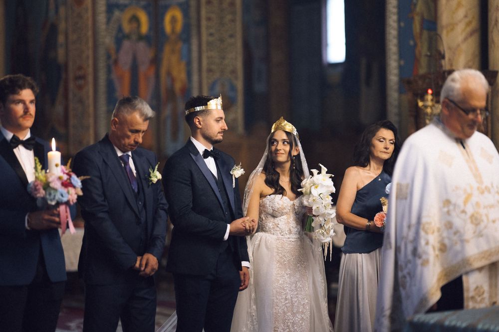 Bride and groom stand at church altar during Orthodox wedding ceremony with guests holding candles.
