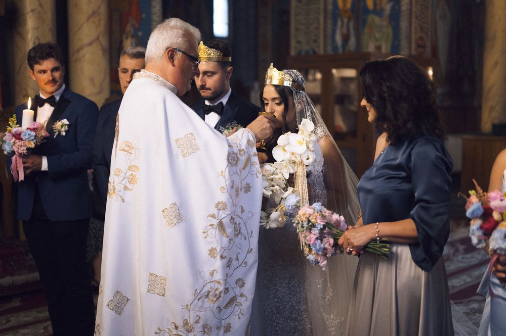 Priest blessing bride in white gown and floral crown during Orthodox church wedding ceremony.