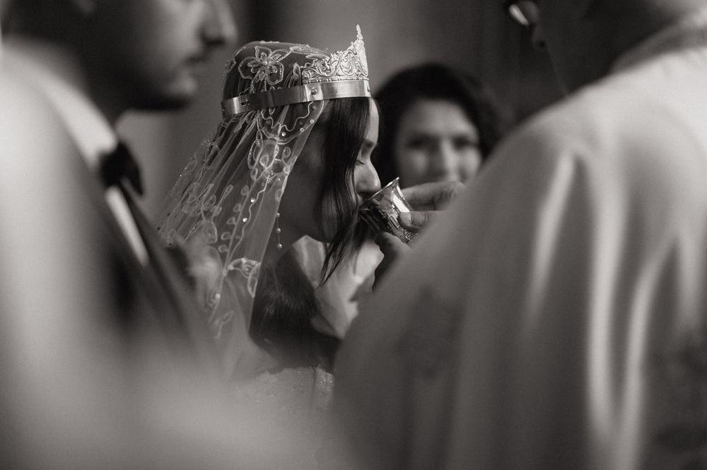 Black and white photo of a bride wearing a crown and veil, kissing a hand during a traditional wedding ceremony.