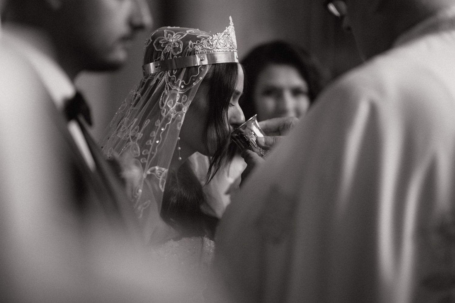 Black and white photo of a bride wearing a crown and veil, kissing a hand during a traditional wedding ceremony.