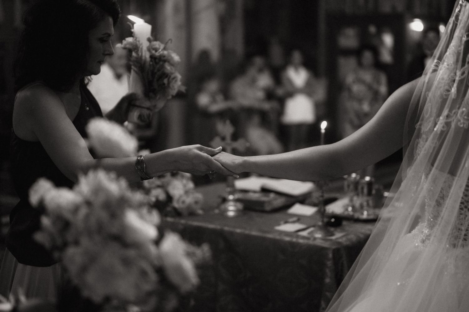 Black and white wedding ceremony photo of bride and officiant exchanging rings at decorated altar with candles and flowers.