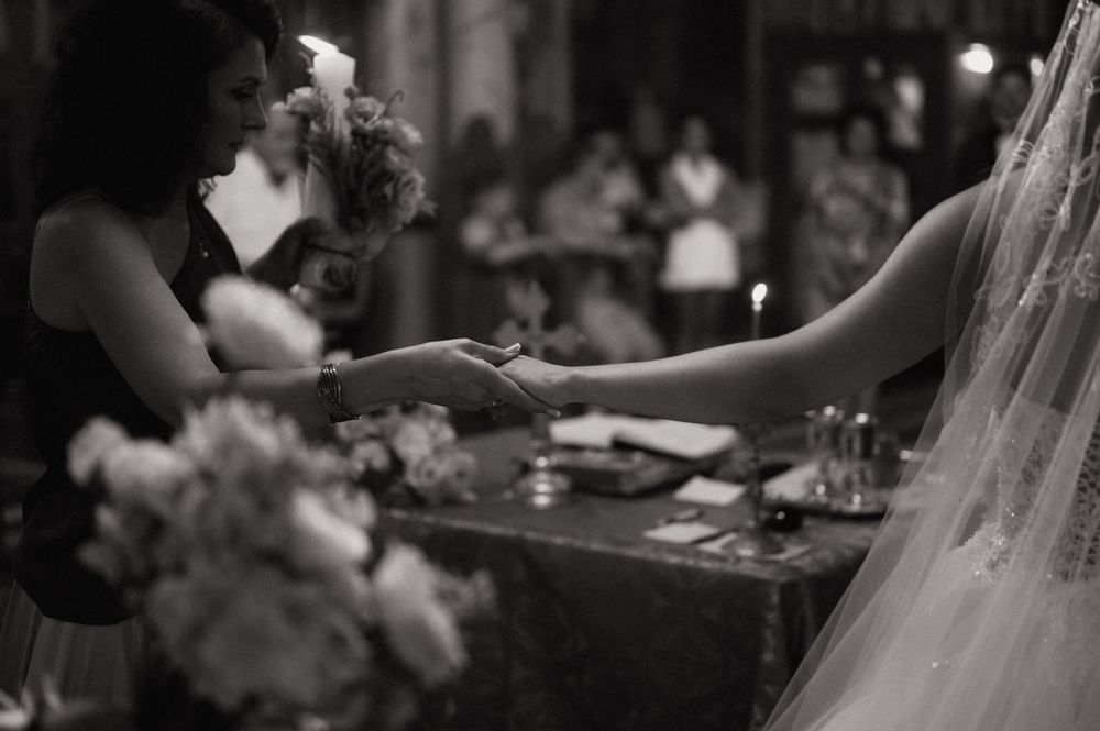 Black and white wedding ceremony photo of bride and officiant exchanging rings at decorated altar with candles and flowers.