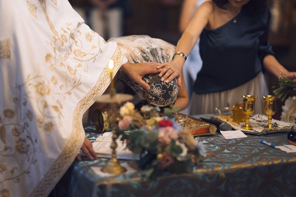 Orthodox priest performing a religious ceremony at an ornate altar with flowers and sacred vessels.